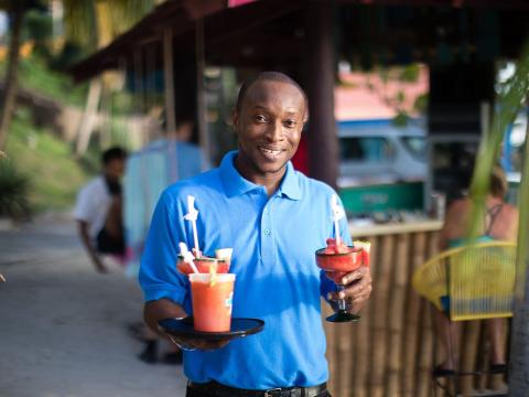 Man in blue shirt serving fruit cocktails at outdoor bar.