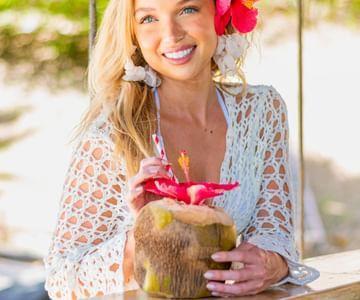 Woman smiling with a coconut drink outdoors adorned with flowers