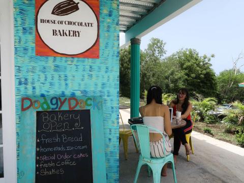 Women chatting at House of Chocolate Bakery with lush background.