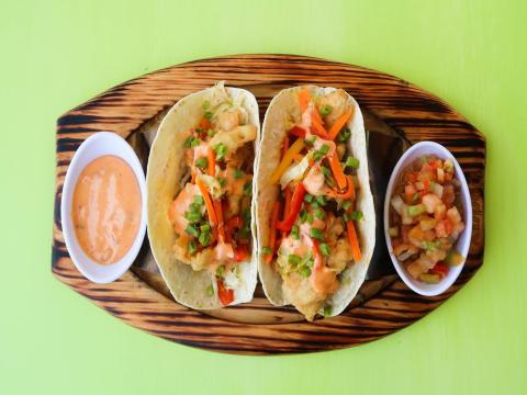 Three fish tortilla wraps with bell peppers, green onions, and two dipping sauces on wooden plate.