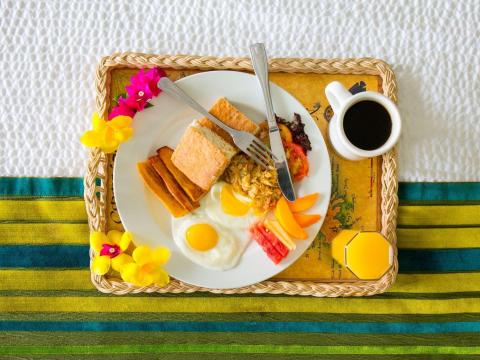 Colorful breakfast tray with eggs, toast, fruits, and coffee on striped tablecloth.