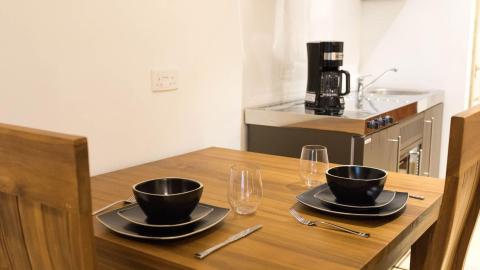 Modern kitchen with a wooden dining set for two, sleek appliances, and gray cabinetry.