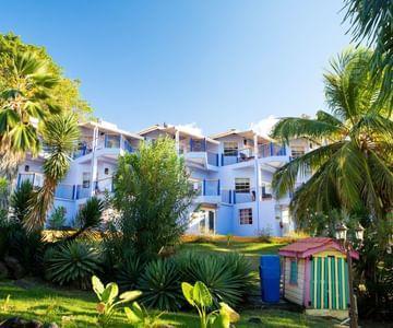 Modern white multi-storey building surrounded by tropical vegetation and colorful beach hut.