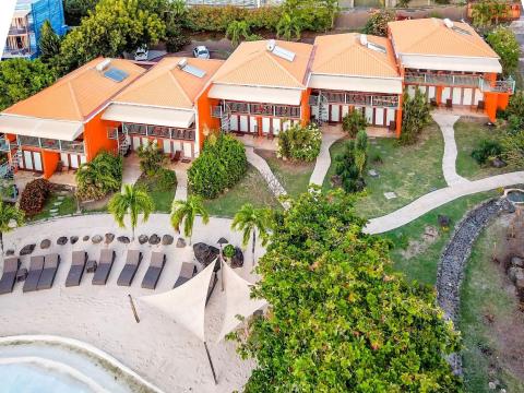Aerial view of a tropical resort with orange-roofed buildings and a sandy lounge area