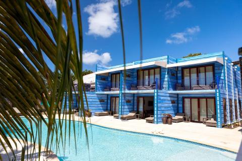 Modern blue resort with pool and balconies surrounded by palm trees on sunny day