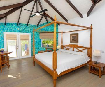 Four-poster bed with white spread in a room with turquoise tile wall and garden view