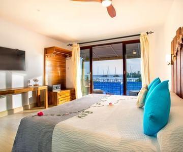 Stylish bedroom with gray bedding, turquoise pillows, and marina view from balcony.