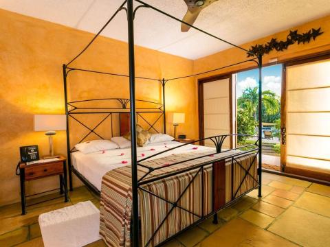 Romantic tropical bedroom with four-poster bed and lush outdoor view.