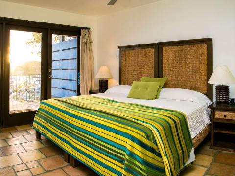 Bright bedroom with green/yellow blanket, terracotta tiles, and balcony view.