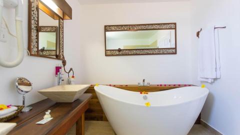Bright, serene bathroom with white tub, wooden fixtures, and rock-framed mirrors.