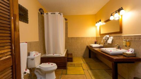 Warmly lit bathroom with bathtub, dual sinks, mirror, and rustic decor.
