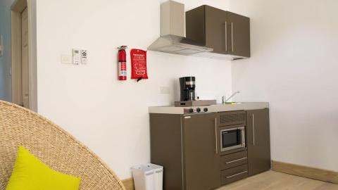Modern kitchenette with yellow pillow on chair, stove, and coffee maker.