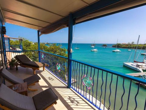 Scenic balcony view of blue sea with sailing boats, sunny day, and relaxing chairs.