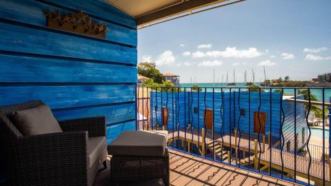 Cozy balcony overlooking marina with sailboats and coastal view under sunny sky.
