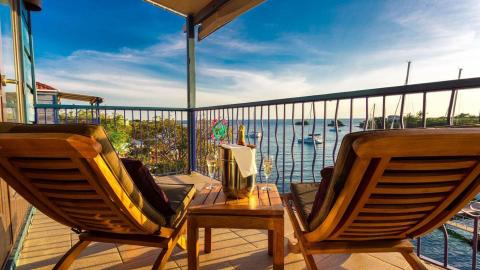 Scenic harbor view from a balcony with chairs, table, champagne, and sunset.