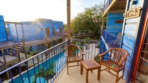 Cozy balcony with wooden chairs overlooking a serene pool and lush surroundings at sunset