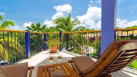 Tropical balcony view with lounge chairs, wine glasses, and green palms on a sunny day.