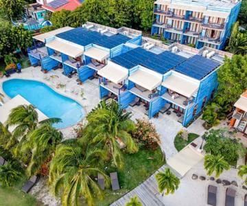 Aerial view of tropical resort with kidney-shaped pool and blue-roofed buildings.