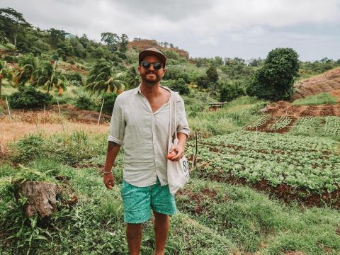 Man in beige shirt and turquoise shorts in lush green agricultural field.