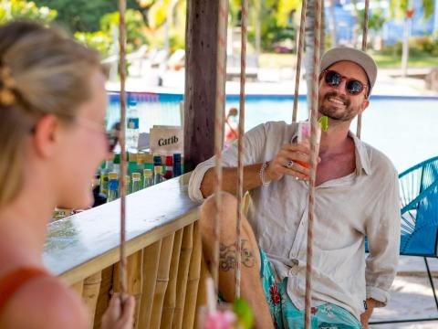 Man and woman enjoying drinks at a tropical bar with lush backdrop