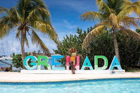 Joyful woman in swimsuit by GRENADA sign at tropical resort