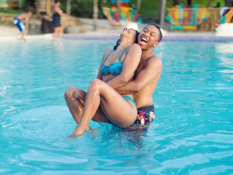 Happy couple playing in a pool with others enjoying nearby