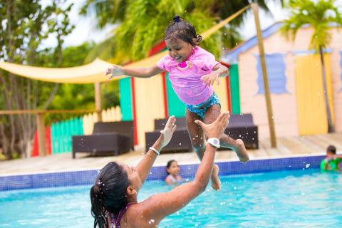 Woman tossing girl in air at pool, splashes around, happy summer vibe