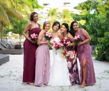 Bride and bridesmaids in pink dresses at beach wedding, joyful and posing