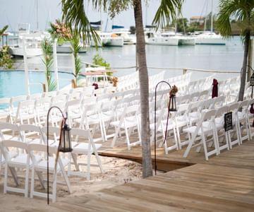 Outdoor wedding setup with white chairs by the harbor under palm trees