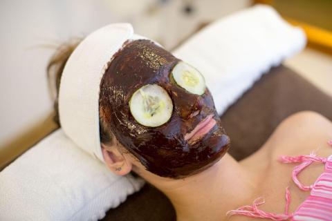 Person with facial mask and cucumber slices on eyes, relaxing at spa