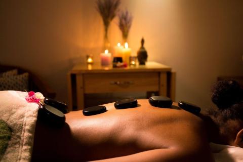Person receiving hot stone massage with candles for a soothing ambiance.