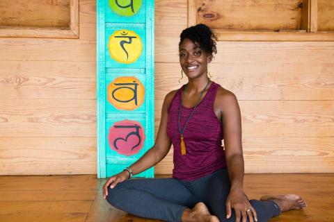 Woman in maroon top meditating on wooden floor with colorful backdrop