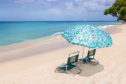 This image shows a tranquil beach scene with a blue and green patterned umbrella and two beach chairs on the sandy shore