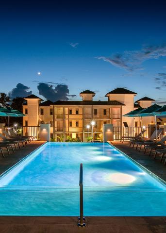 This image depicts a beautifully illuminated outdoor swimming pool during the evening or early night time