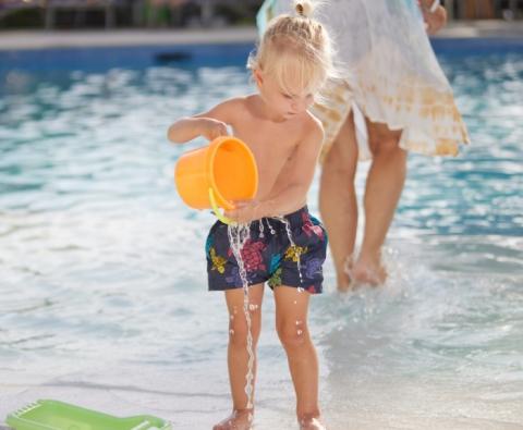 The image captures a young child playing with water by a poolside