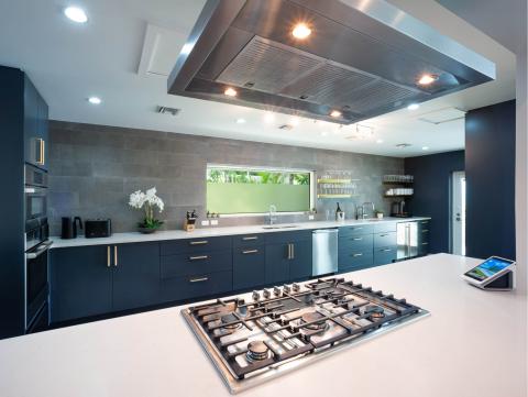 This image shows a modern kitchen interior featuring a large stainless steel gas stove top, prominent overhead exhaust hood, and sleek dark blue cabinetry