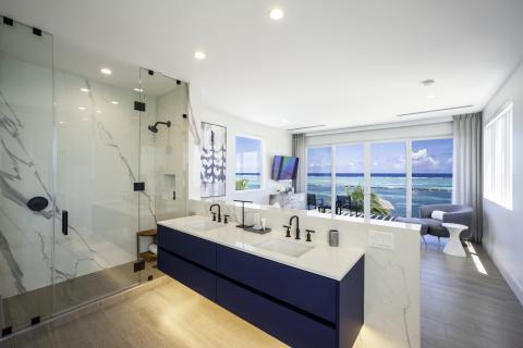 This image shows a luxurious bathroom with a modern design, featuring a large glass-walled shower at the left and a long vanity with dual sinks and a navy blue base