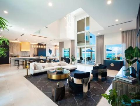 This image shows a modern and luxurious living room interior with high ceilings and an open plan layout that integrates into a kitchen area