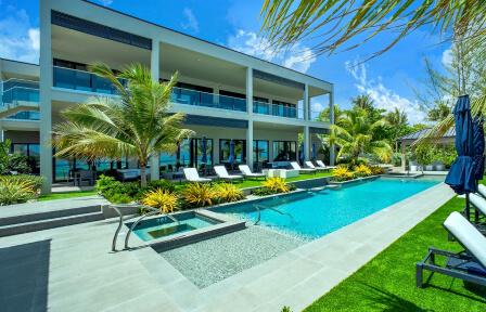 The image shows a modern luxury villa with a large swimming pool in the foreground