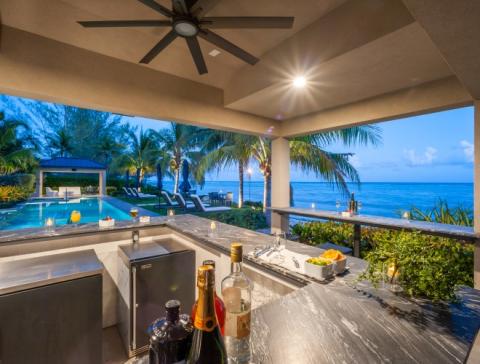 This image captures an elegant outdoor kitchen and bar area overlooking a scenic beach setting