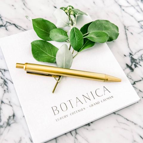 This image features a promotional or presentation setup that involves a booklet with the text "BOTANICA, Luxury Cottages, Grand Cayman" printed on its cover