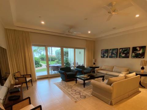 The image shows a well-furnished living room with large windows that provide a view of a meticulously landscaped garden and patio area