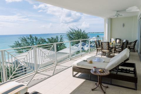 The image shows a spacious and elegant outdoor balcony with a stunning view of the ocean