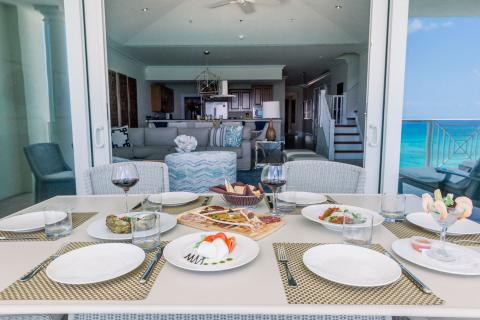 This image shows a beautifully set dining table on a patio with a clear view of the ocean