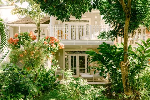 This image features a lush garden in front of a beautiful building that has a tropical architectural style