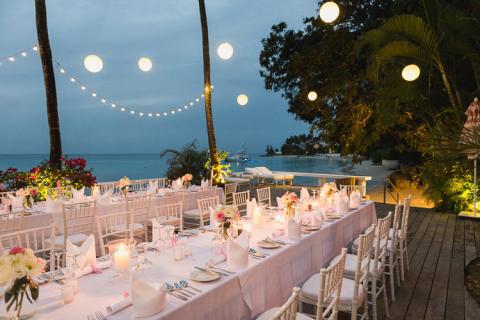 This image depicts an elegantly set outdoor dining area in a beachside setting during the evening