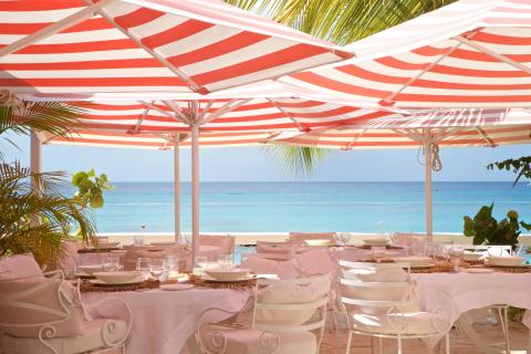 This image captures an elegant beachfront dining setup under red and white striped umbrellas