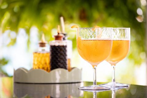 The image features two stemmed cocktail glasses filled with a bubbly, orange-colored liquid, possibly a type of cocktail or sparkling beverage