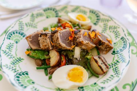 This image shows a beautifully arranged dish consisting of seared tuna steak slices served on a bed of green leafy salad with a variety of vegetables