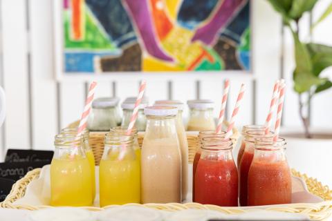 The image shows an array of freshly prepared beverages served in glass jars, each fitted with a pink and white striped drinking straw